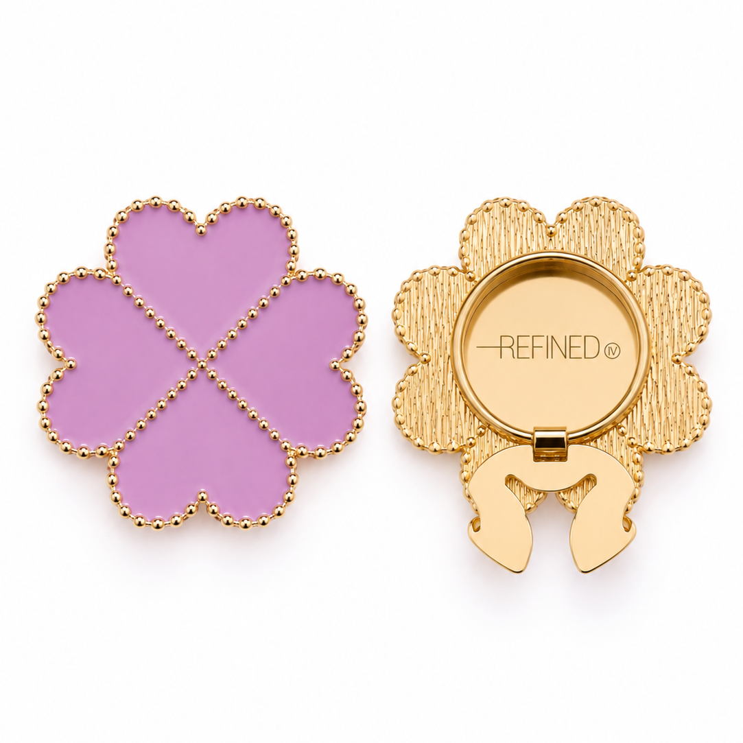 A four-leaf clover-shaped gold-tone decorative button cover with mauve lilac-pink heart-shaped sections and a gold-dotted outline, shown closed and open on a white background. Refined by JV branding is visible on the back beside the clip-on clasp mechanism