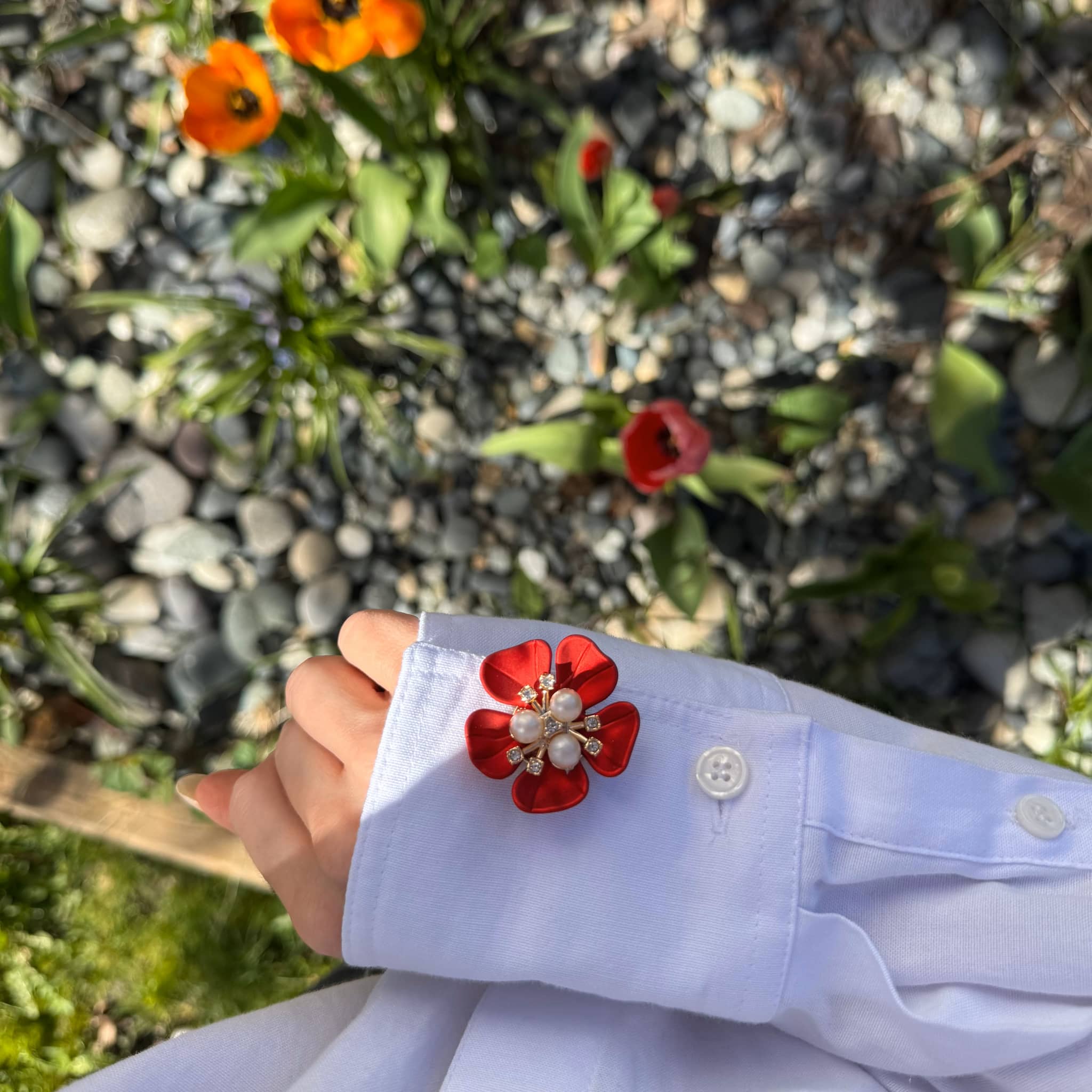Refined by JV crimson flower button cover with pearl center attached to a white shirt cuff in a garden setting
