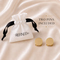 Refined by JV gold-tone button cover pins with a branded white drawstring pouch on a soft satin background.
