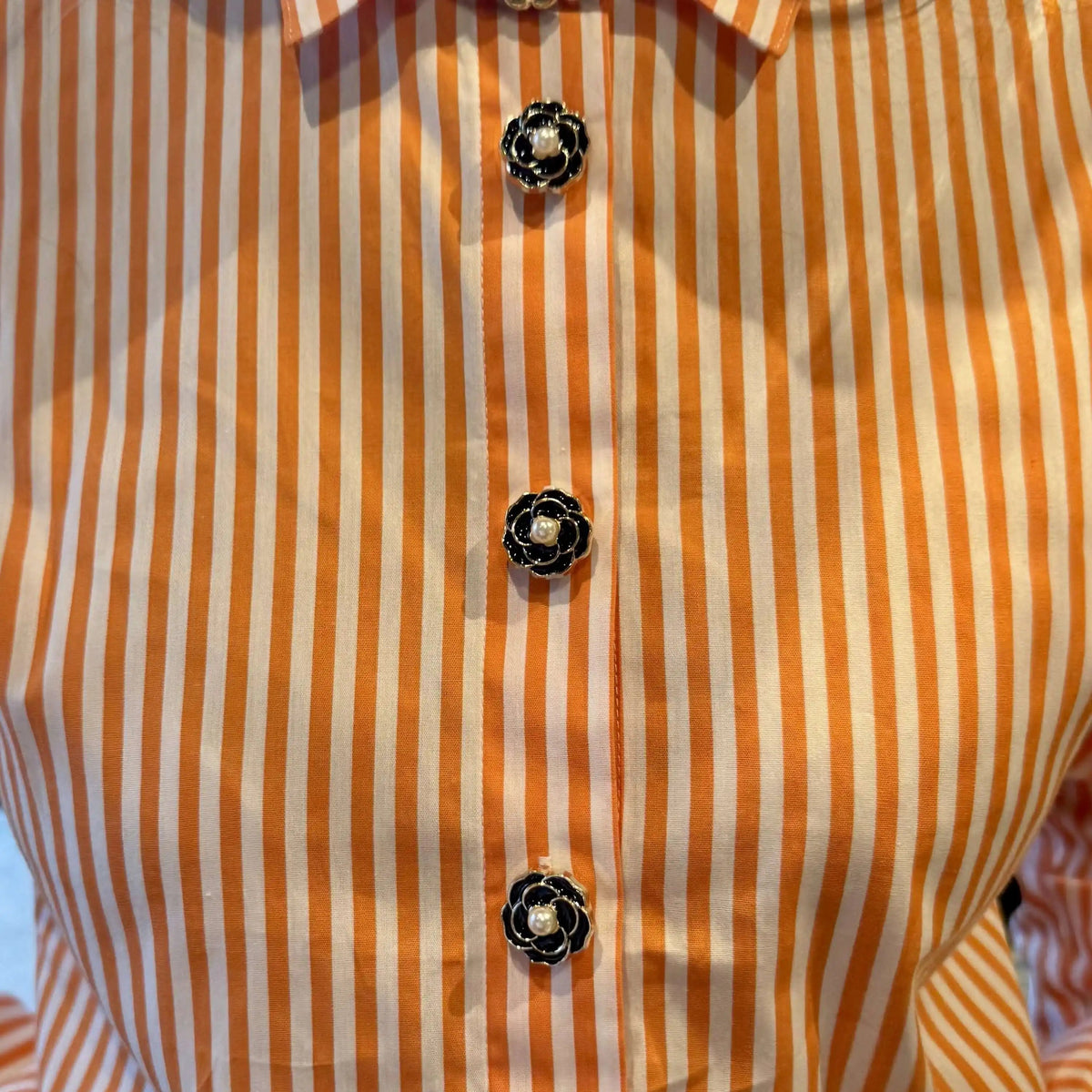 Refined by JV Noir Camélia button covers featuring black enamel, gold frames, and pearl centers on a striped shirt.