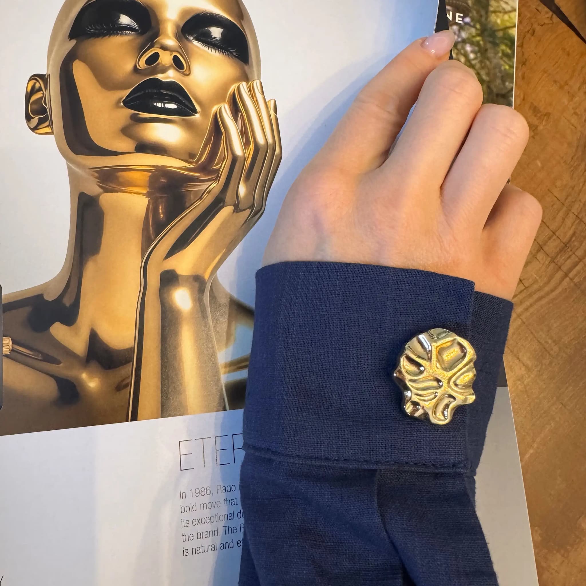 Refined by JV gold-tone sculpted button cover attached to a navy blue shirt cuff with an organic, modern design.